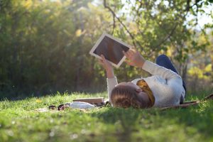 Woman Lying On Bedding On Green Grass With Ipad During Picknic I